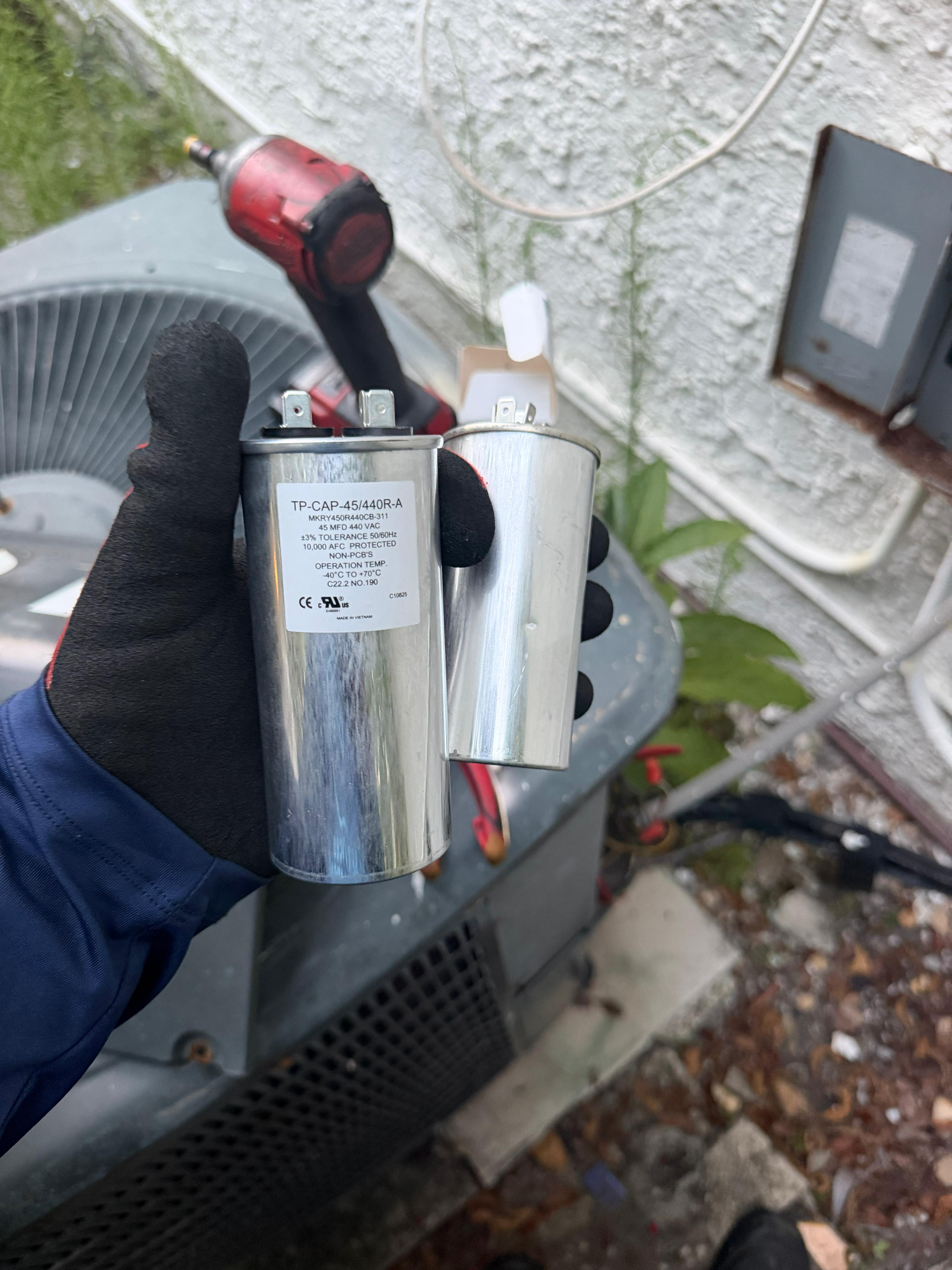 Cooling Masters technician holding old and new capacitor — capacitor replacement job