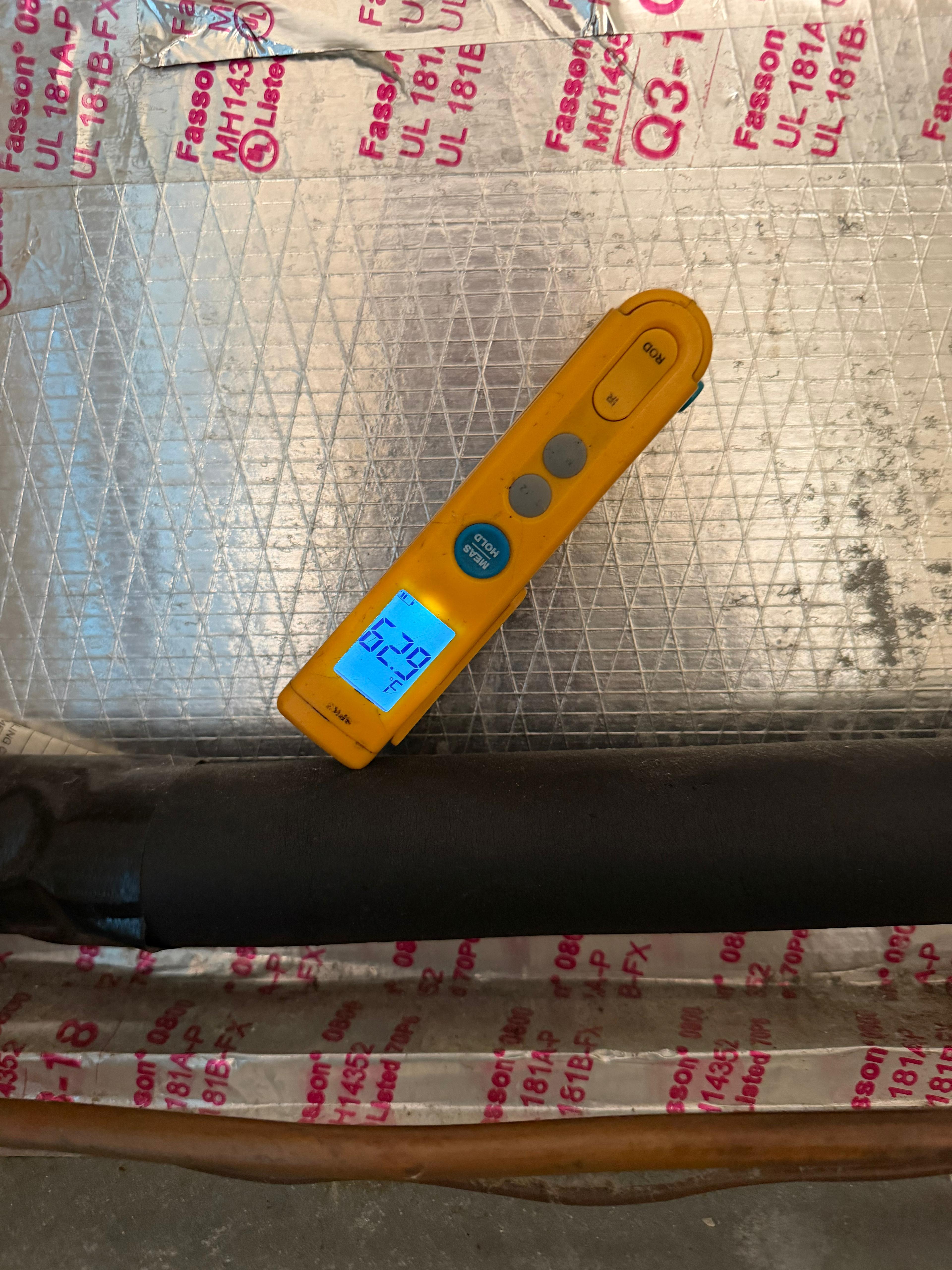 Digital thermometer reading 52°F in AC plenum — supply air temperature test